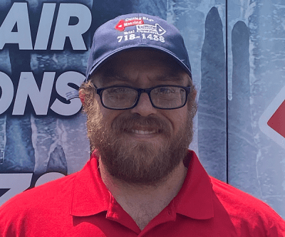 Man in glasses and red polo shirt smiling in front of a blue sign, wearing a dark baseball cap