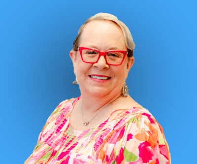 Smiling person wearing red glasses and a floral top against a blue background