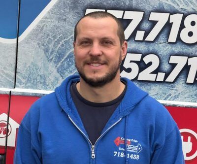 Man in blue zip-up jacket smiling in front of a vehicle with large white numbers.