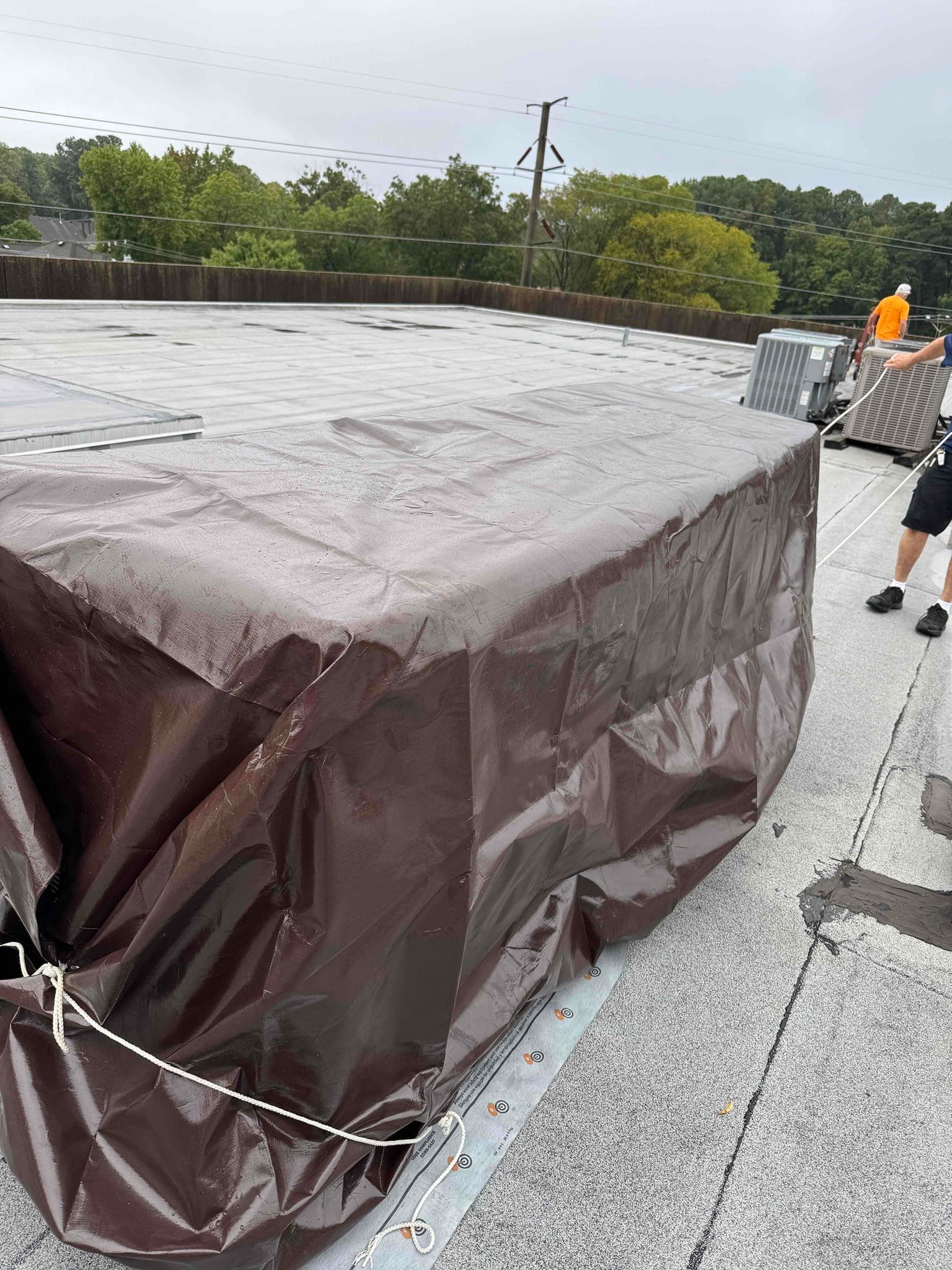 Large dark tarped rooftop structure with a worker in orange safety gear on a flat roof