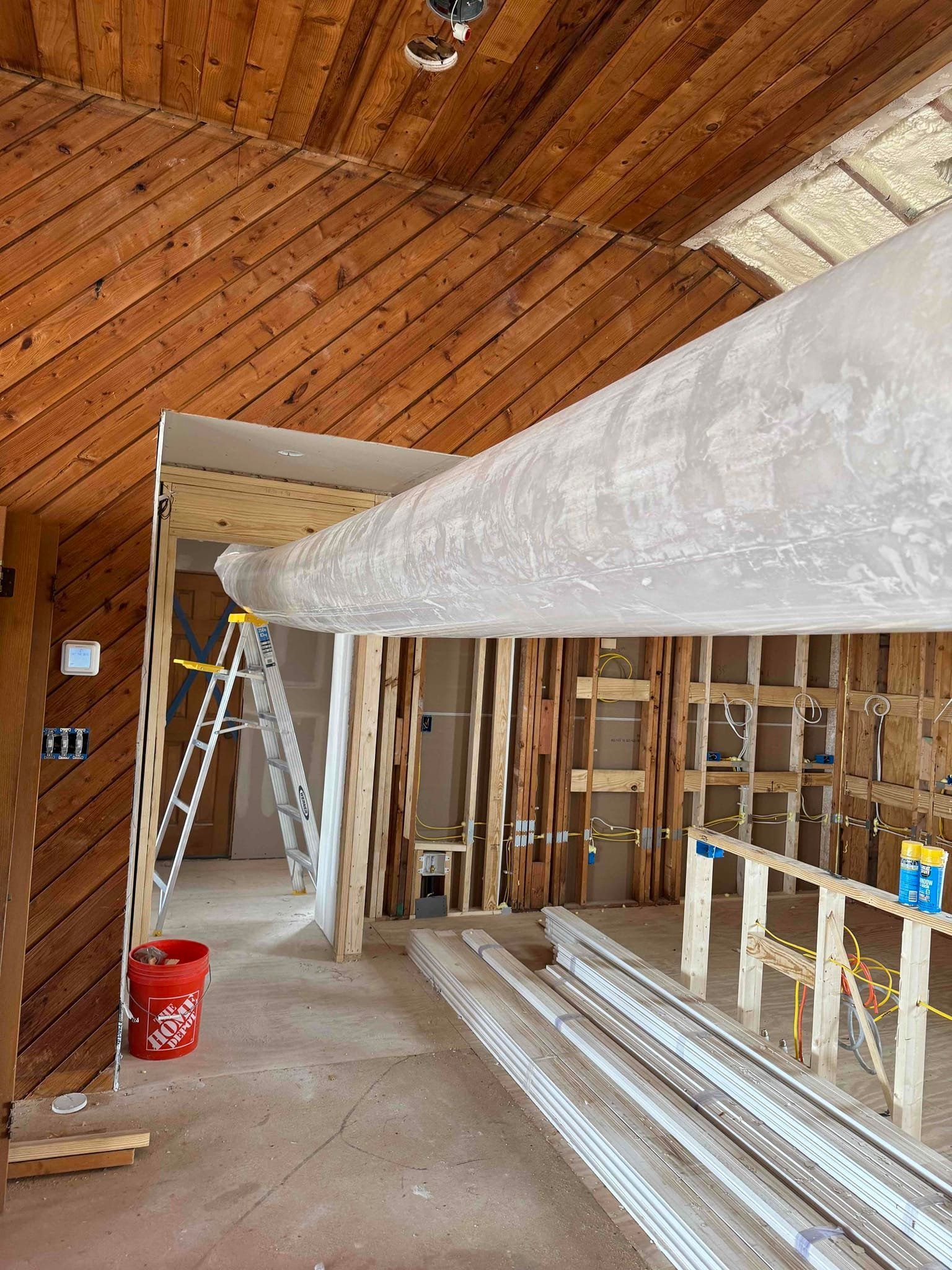 Partially renovated room with exposed framing, ladder, and drywall materials under a wood ceiling