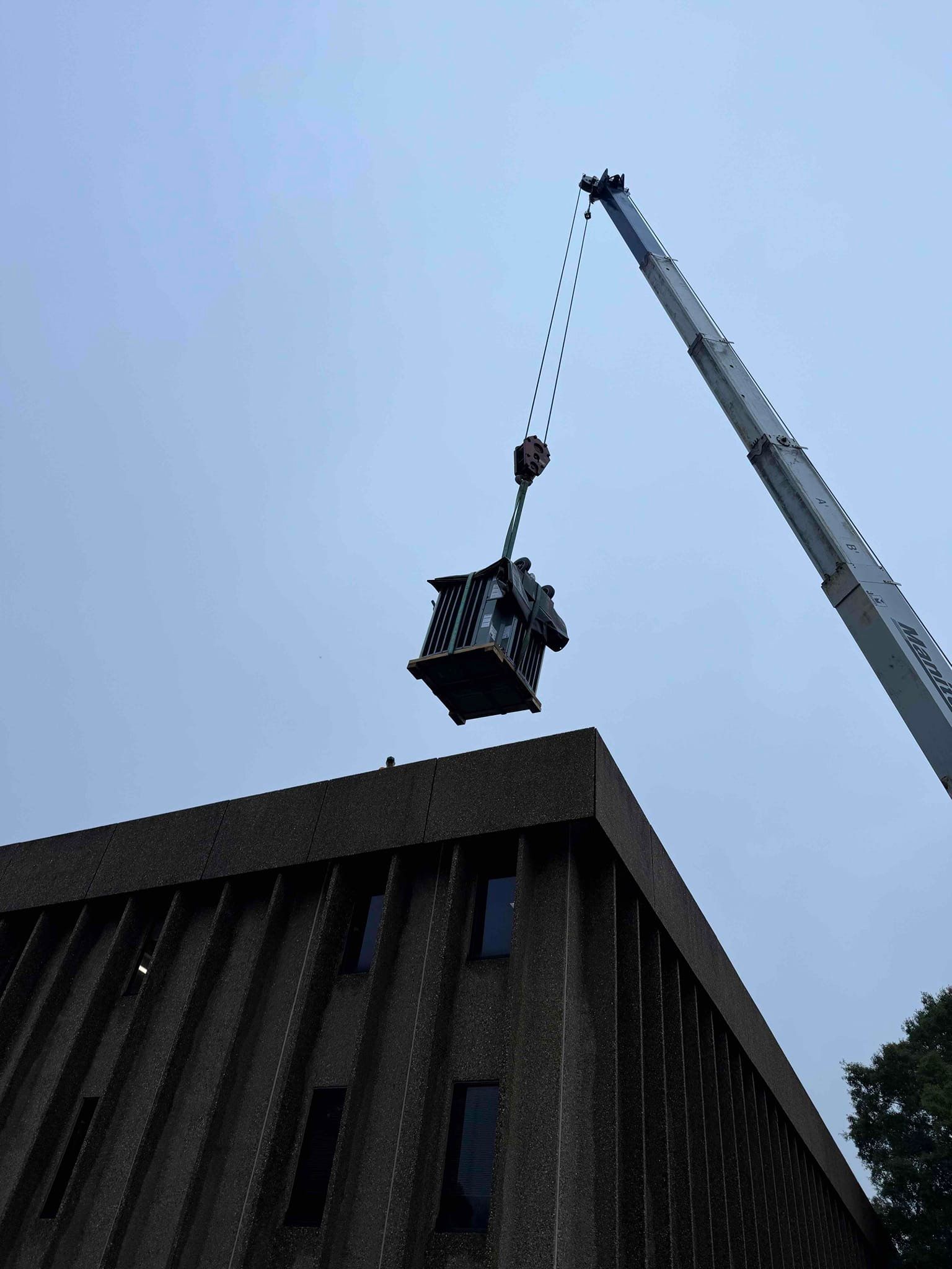 Crane lifting a heavy load above a dark rooftop against a gray sky