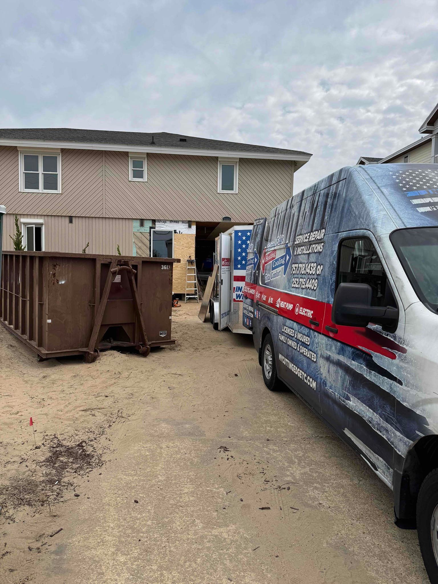 Service van parked beside a dumpster in a gravel alley behind a house, with a fence and cloudy sky.