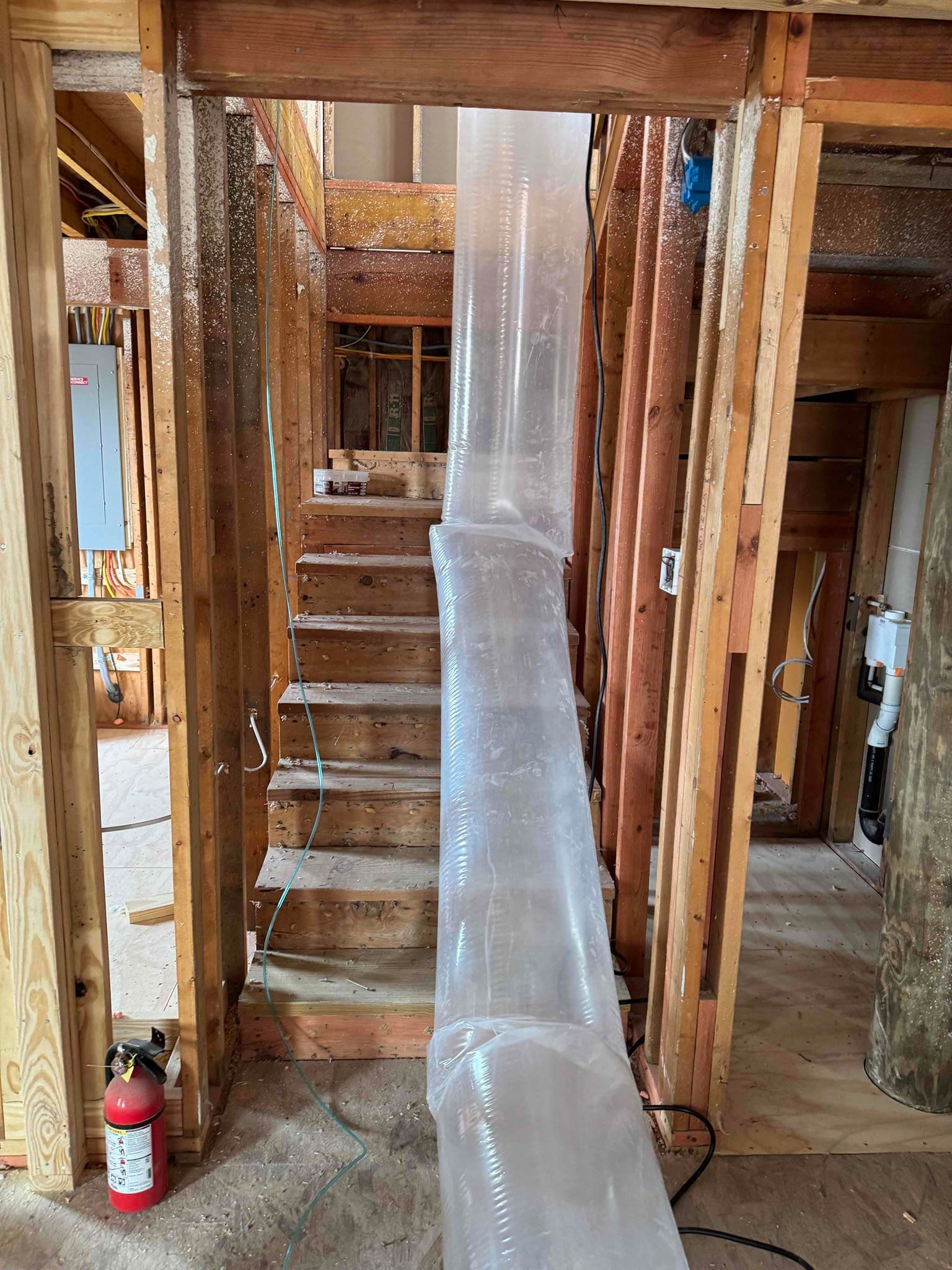 Construction site with a plastic-covered stairwell framed by exposed wooden studs.