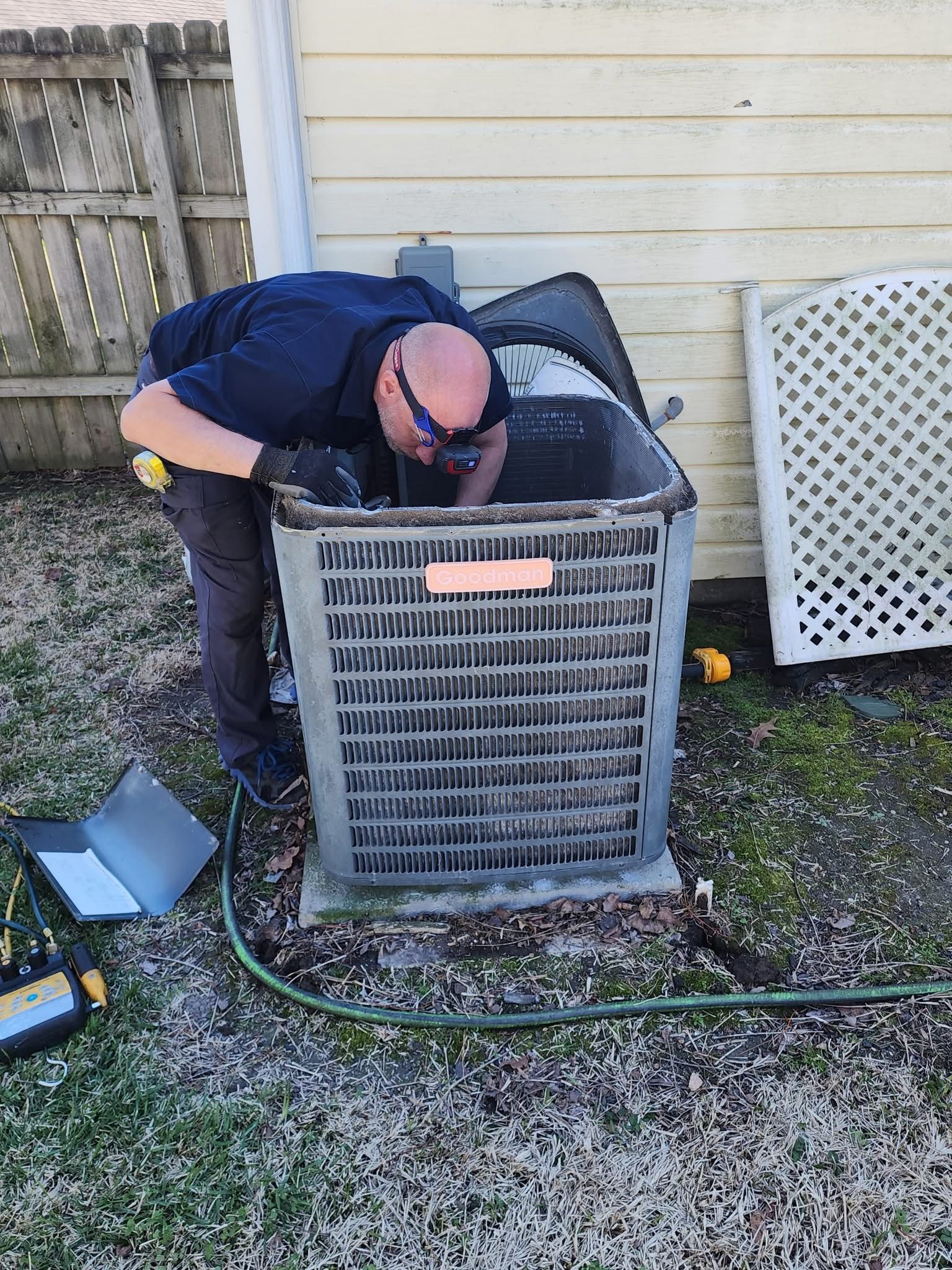 Technician inspecting an outdoor air conditioner unit beside a house.