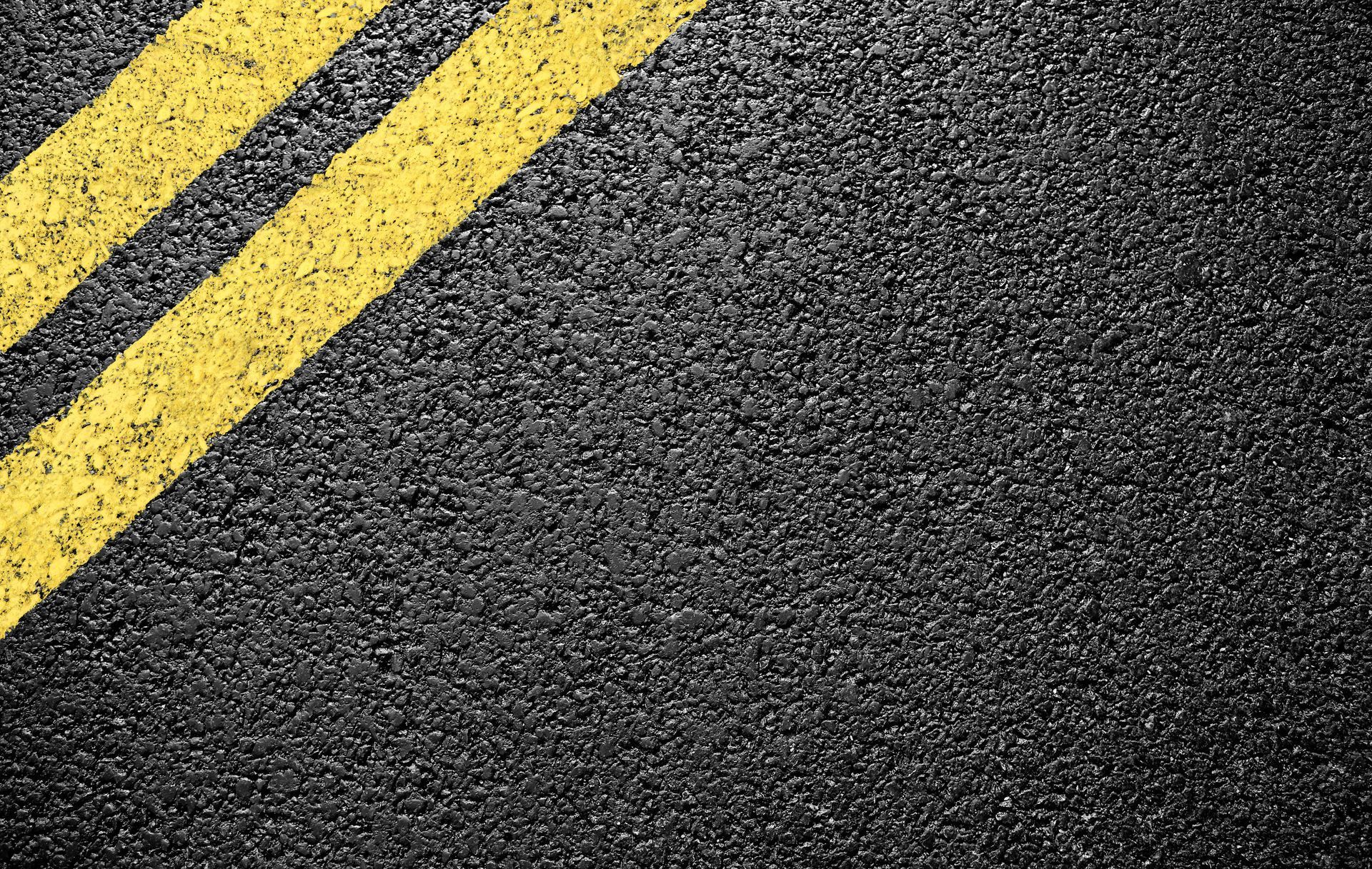 Black asphalt road with diagonal yellow double lines.