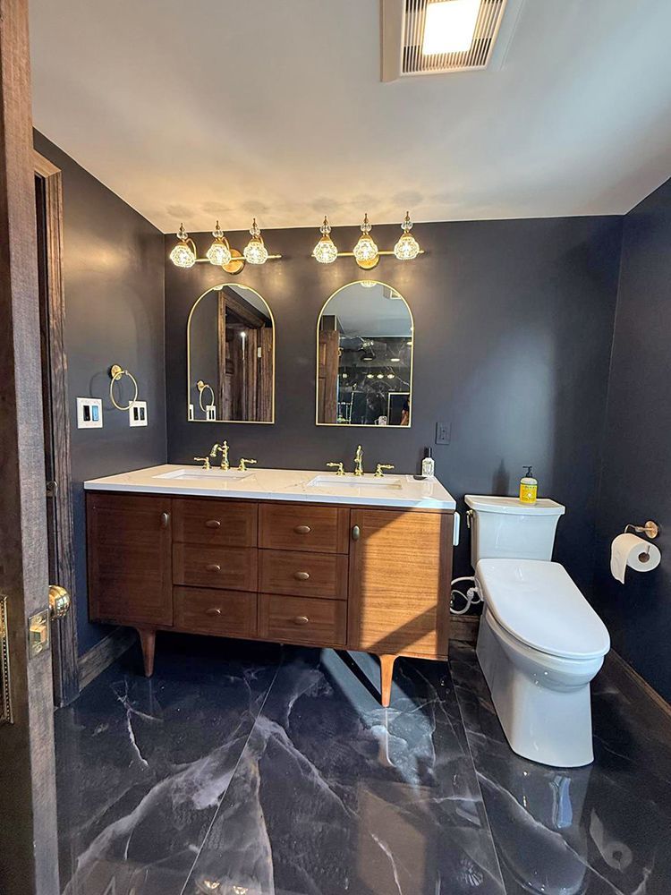 Bathroom with a dark blue wall, marble floor, wood vanity, and gold accents.