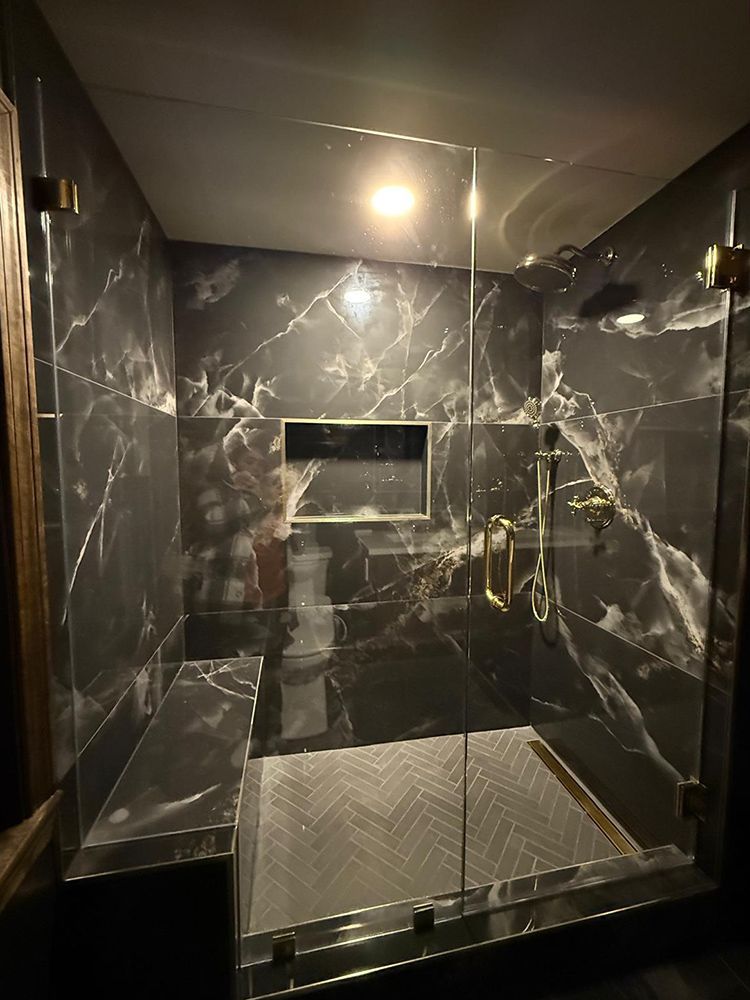 Luxurious shower with black marble tile, gold fixtures, and glass doors.