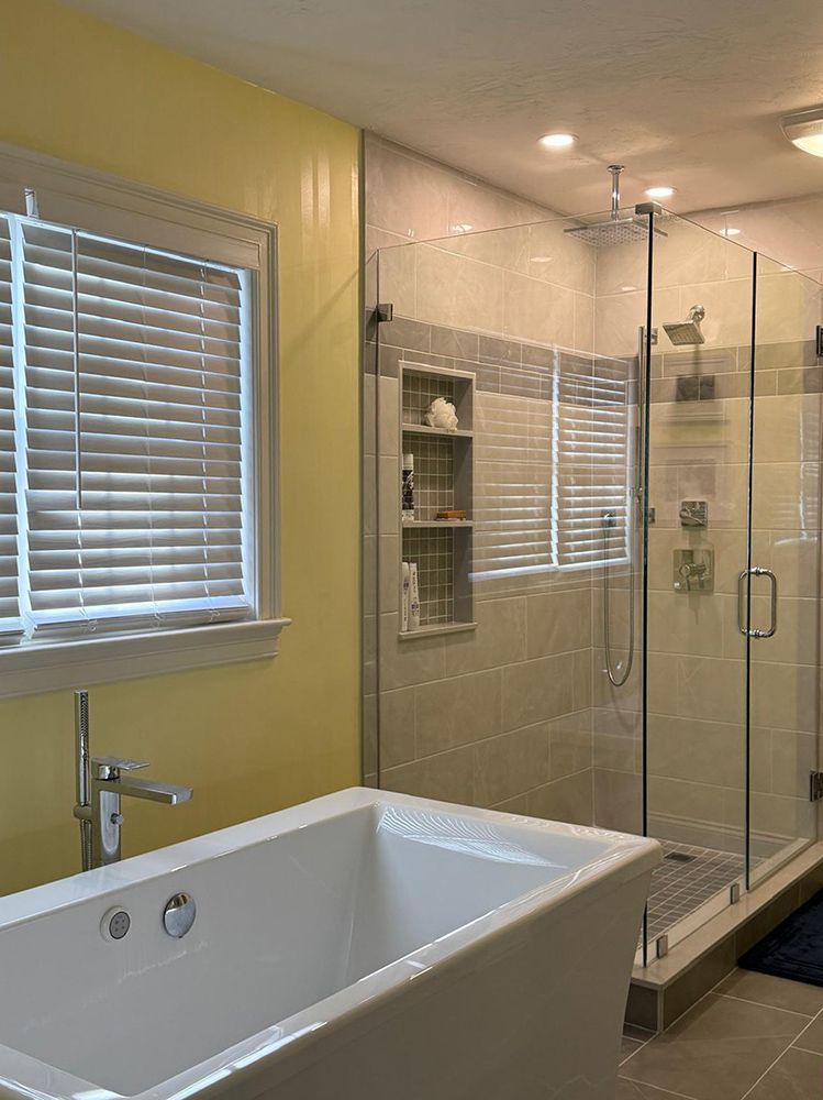 Bathroom with a freestanding tub, glass shower, yellow walls, and a window with blinds.