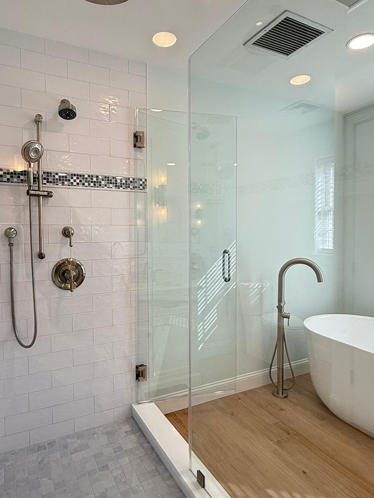 Modern bathroom: glass shower, white tub, wooden floor.