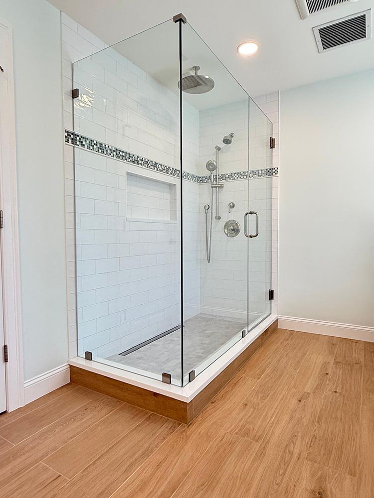 Modern shower with glass enclosure, white tile walls, and wood-look flooring.