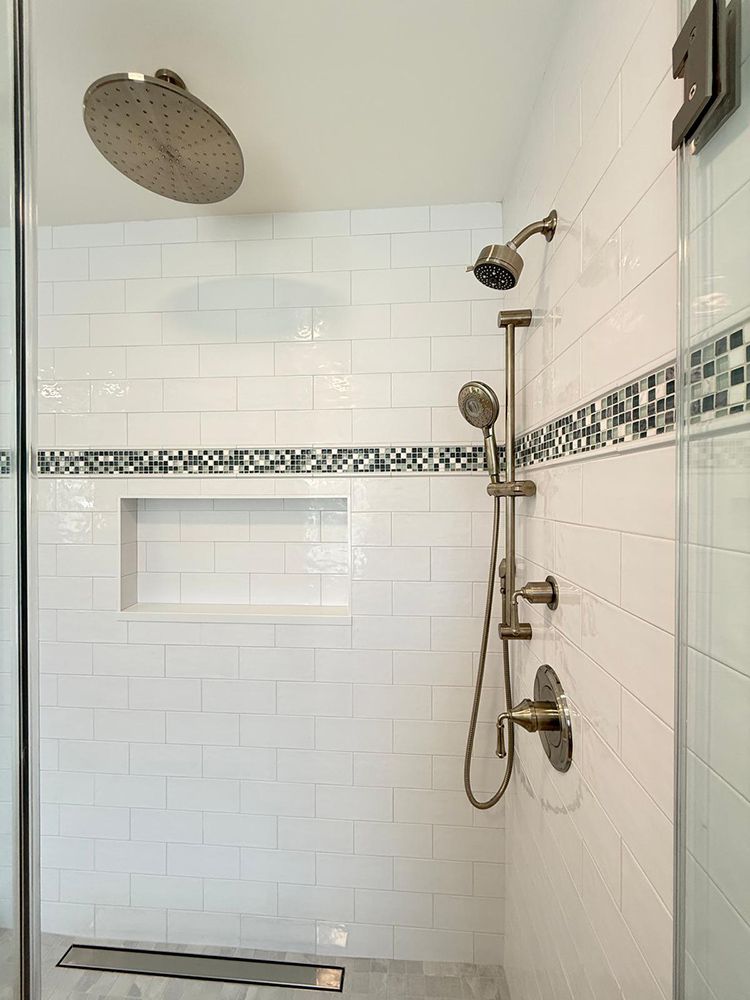 Modern white tile shower with rain shower head and handheld, niche, and glass door.