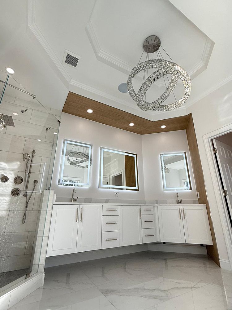 Modern bathroom with white cabinets, large mirrors, and a crystal chandelier.