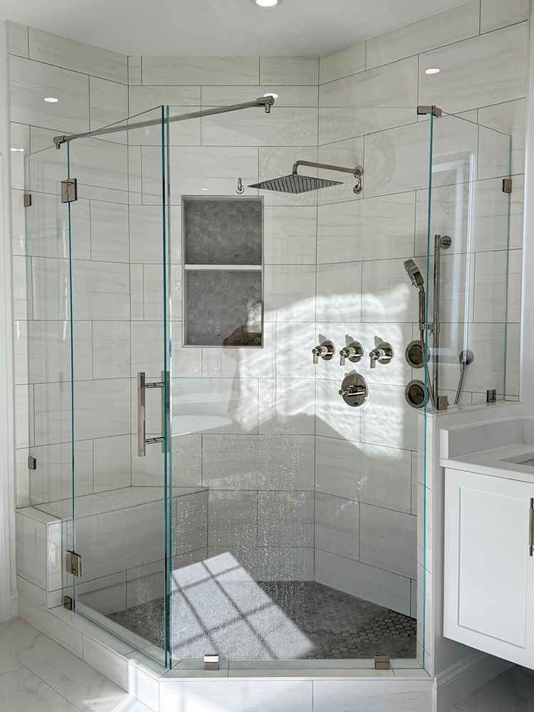 Glass shower enclosure with white tile walls, gray stone floor, and chrome fixtures.
