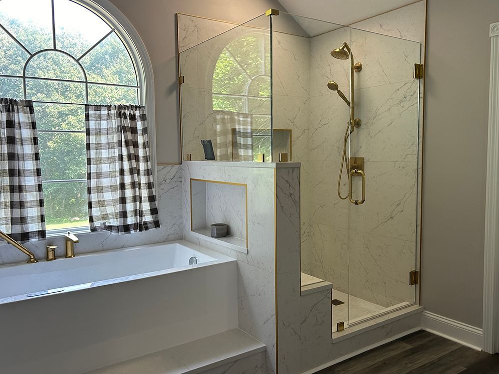 Bathroom with white marble, gold fixtures, glass shower, and checkered window curtain.