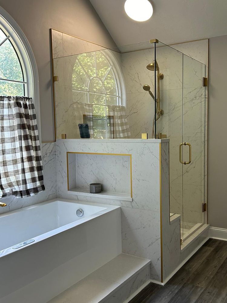 Modern bathroom with marble-look tile, glass shower, gold fixtures, and a soaking tub.