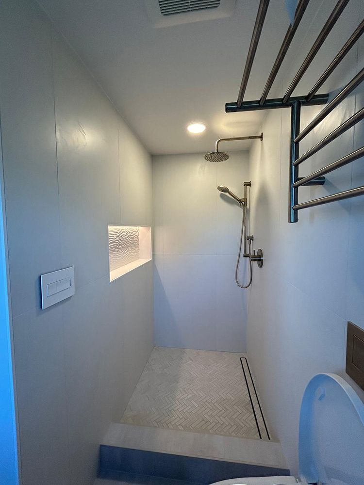 Narrow bathroom with showerhead, shelf, and clothes rack. Grey walls, white tile.