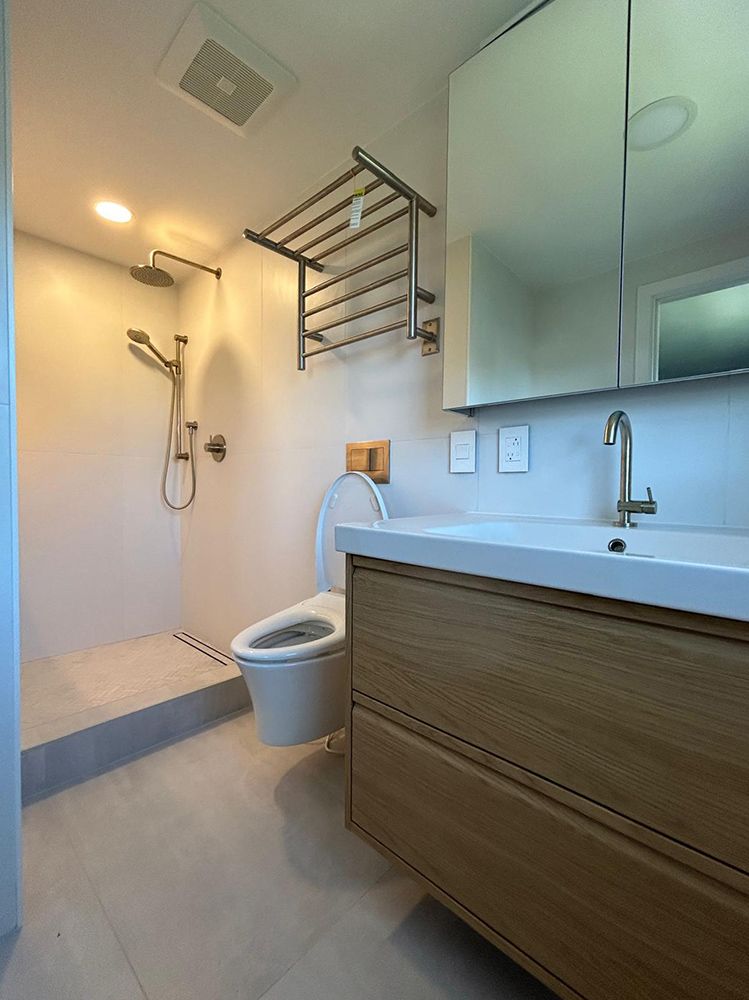 Modern bathroom with walk-in shower, wooden vanity, toilet, towel rack. Neutral tones, bright lighting.