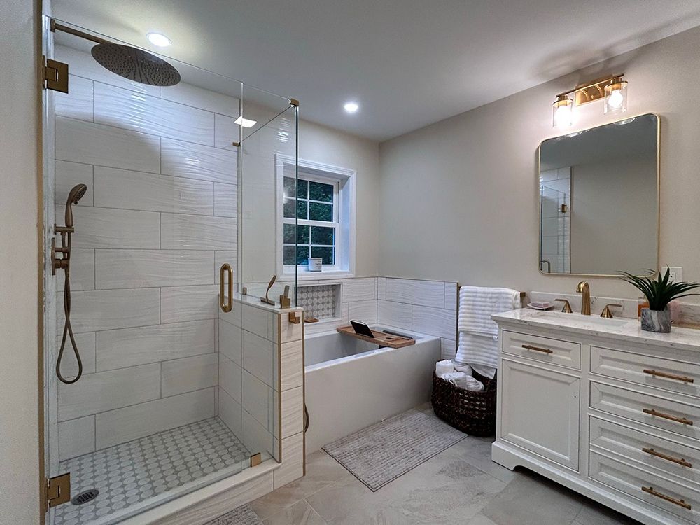 Modern bathroom with a white shower, tub, vanity, and gold accents.