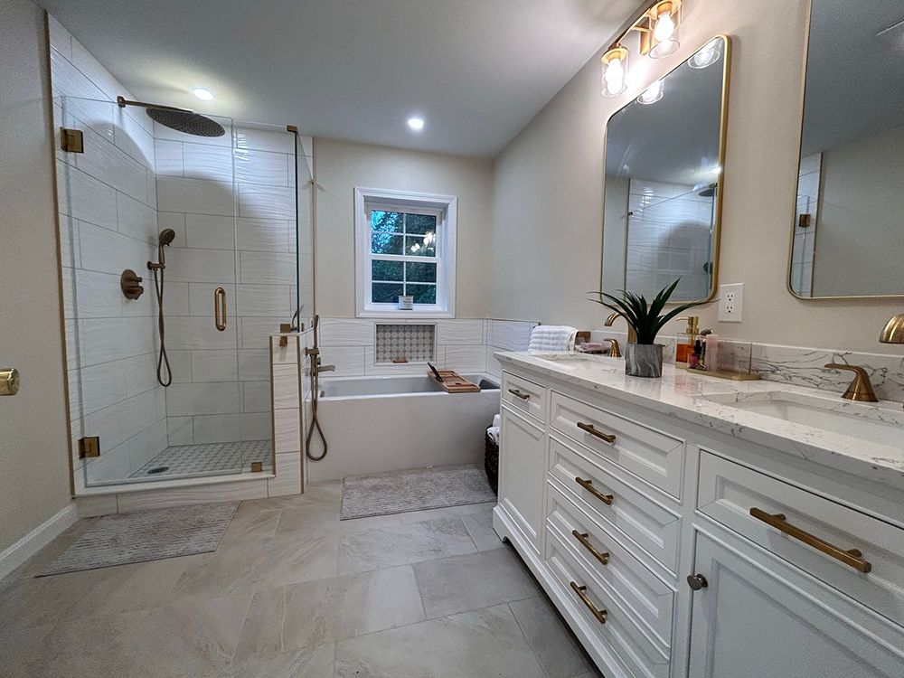 Elegant white bathroom with a shower, vanity, bathtub, and gold fixtures.