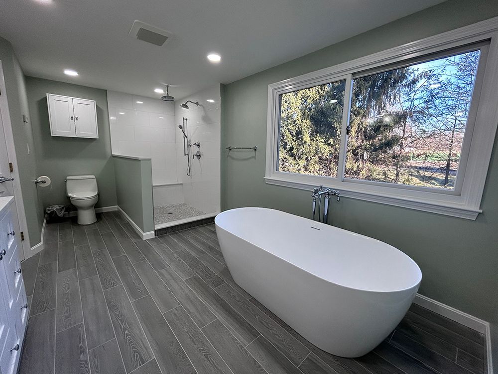 Modern bathroom with freestanding tub, walk-in shower, toilet, gray floor, and window with outdoor view.