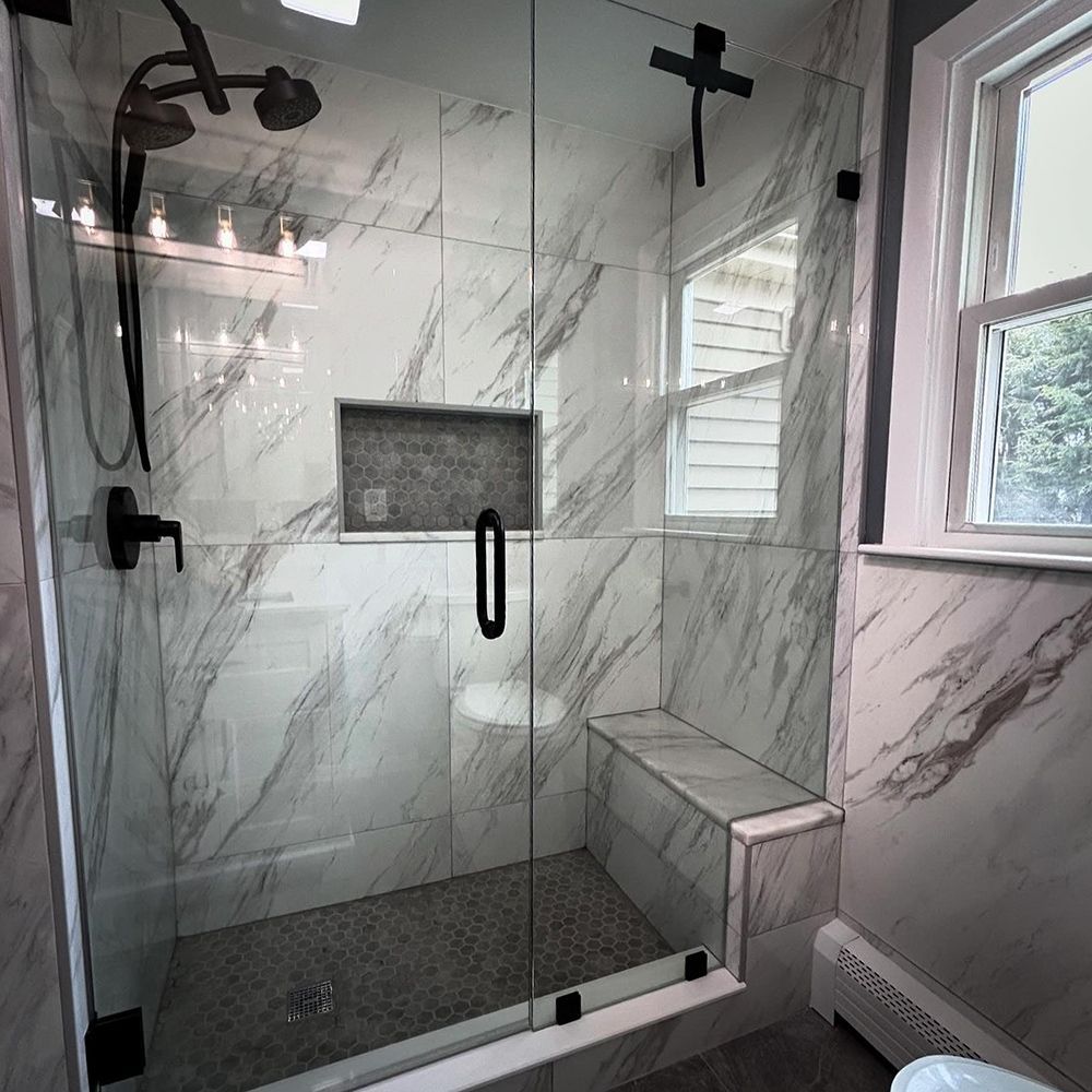 Modern bathroom with marble tile, glass shower door, black fixtures, and a bench.