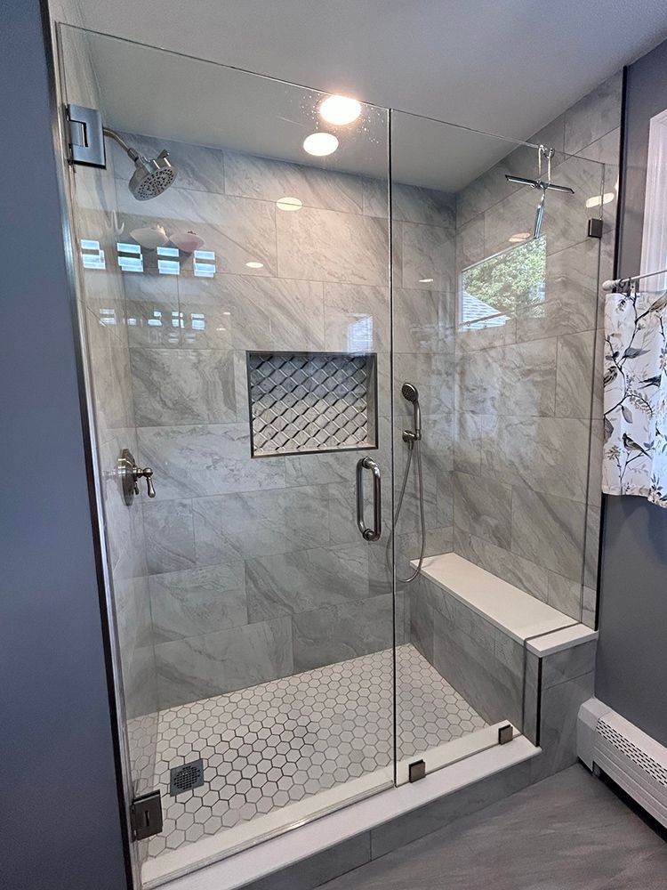 Modern glass shower with gray tile walls, a built-in bench, and a hexagon tile floor.