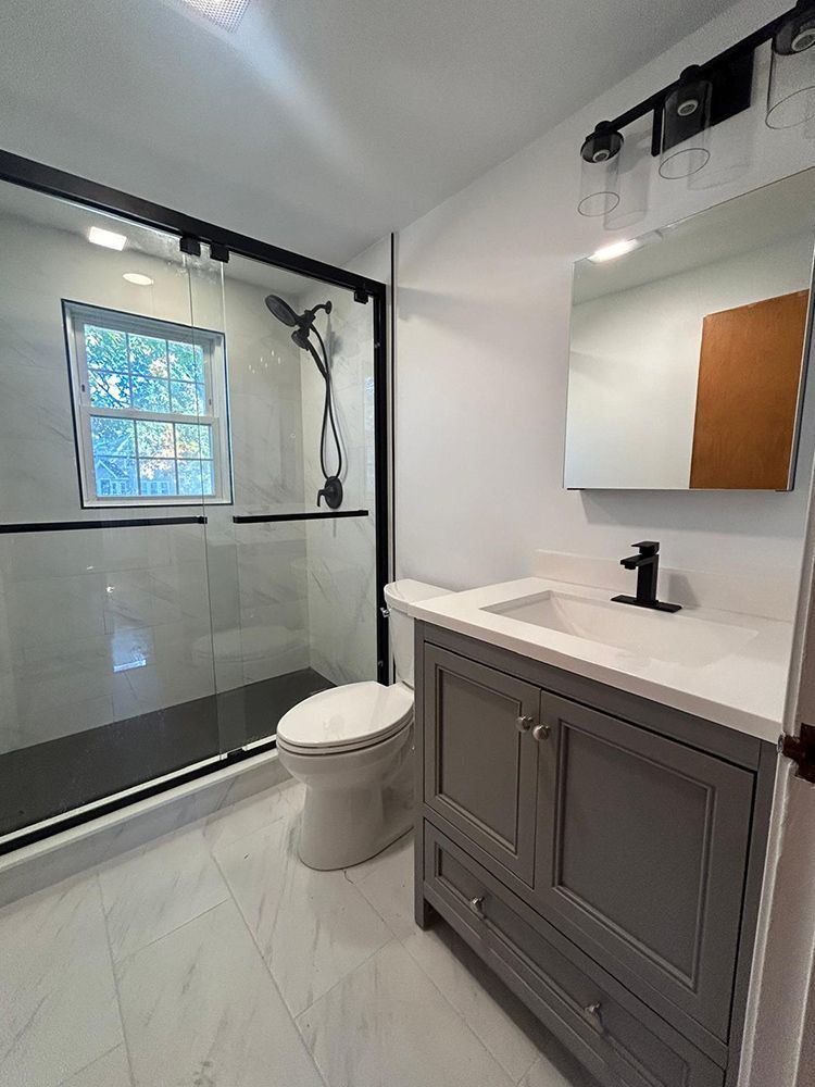 Bathroom with gray vanity, glass shower, and white tile.