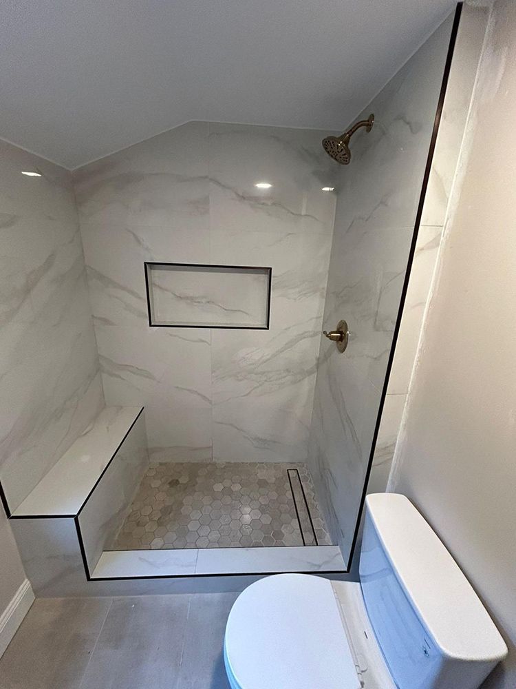 Newly renovated bathroom with marble-look shower, built-in bench, and recessed shelf. A toilet is in view.