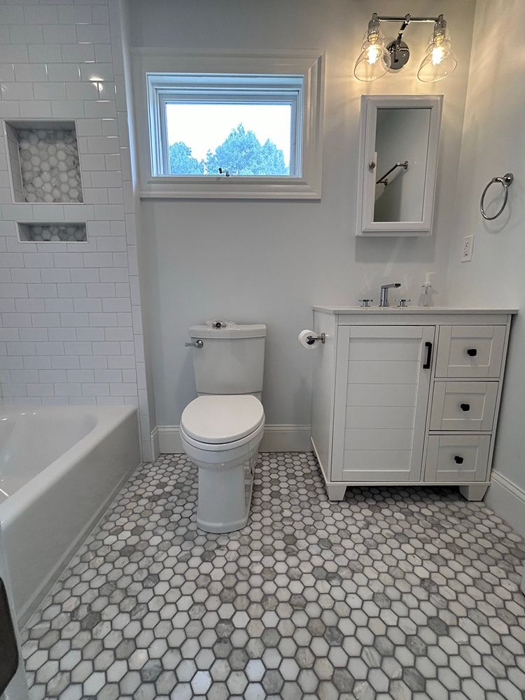 Bathroom with white and gray hexagonal floor tiles, white vanity and toilet, and a window.