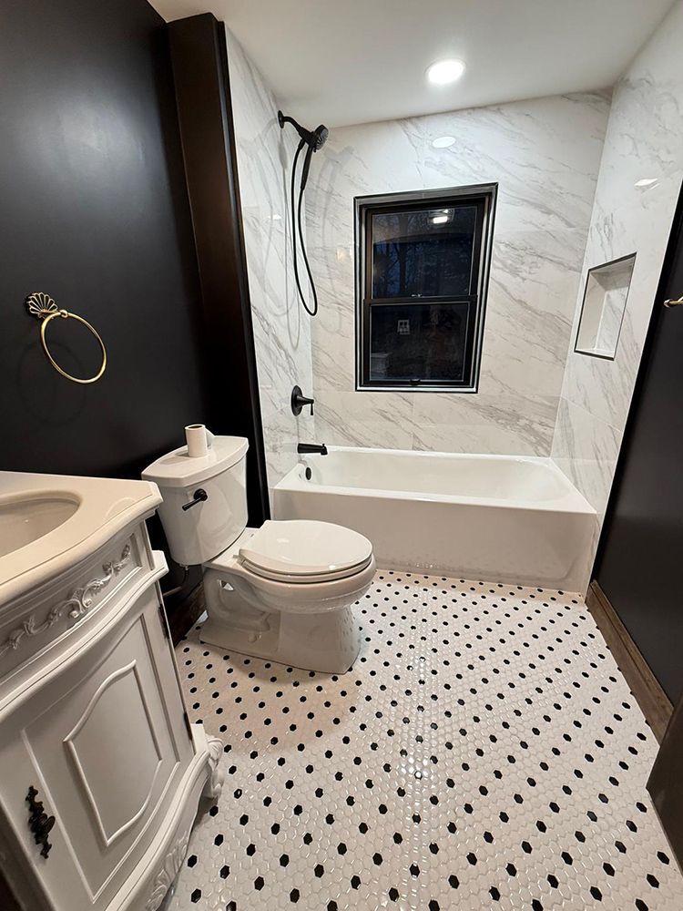 Bathroom with white marble tile, black and white mosaic floor, black accent wall, and white vanity.