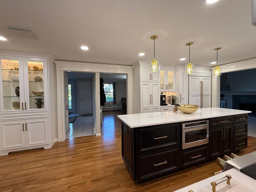 Kitchen with dark island, white cabinets, gold pendant lights, and hardwood floors.
