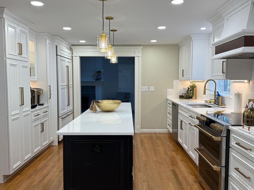 White kitchen with black island, gold accents, wood floors, and recessed lighting.