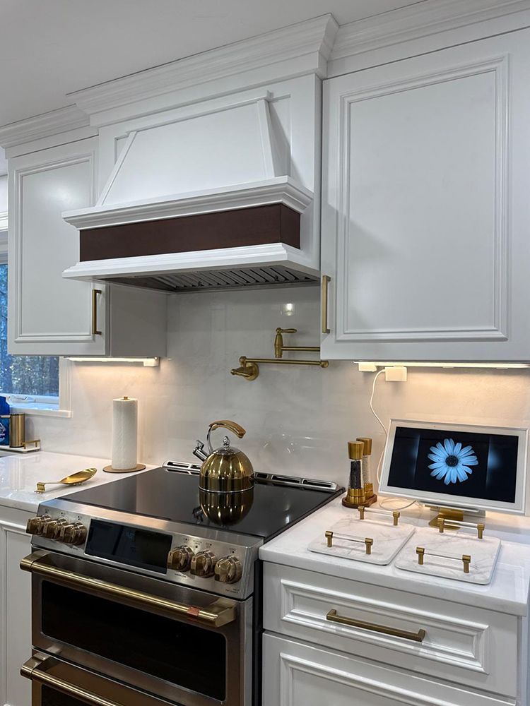 White kitchen with gold accents: stove, kettle, faucet, cabinets, and range hood.