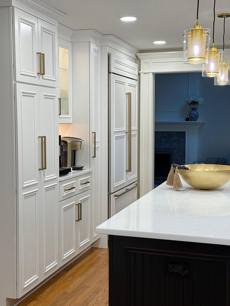 White kitchen cabinets with gold hardware, countertop, black island, and hanging lights.