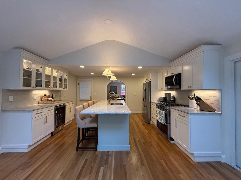White kitchen with island, cabinets, and appliances, hardwood floor, and neutral walls.