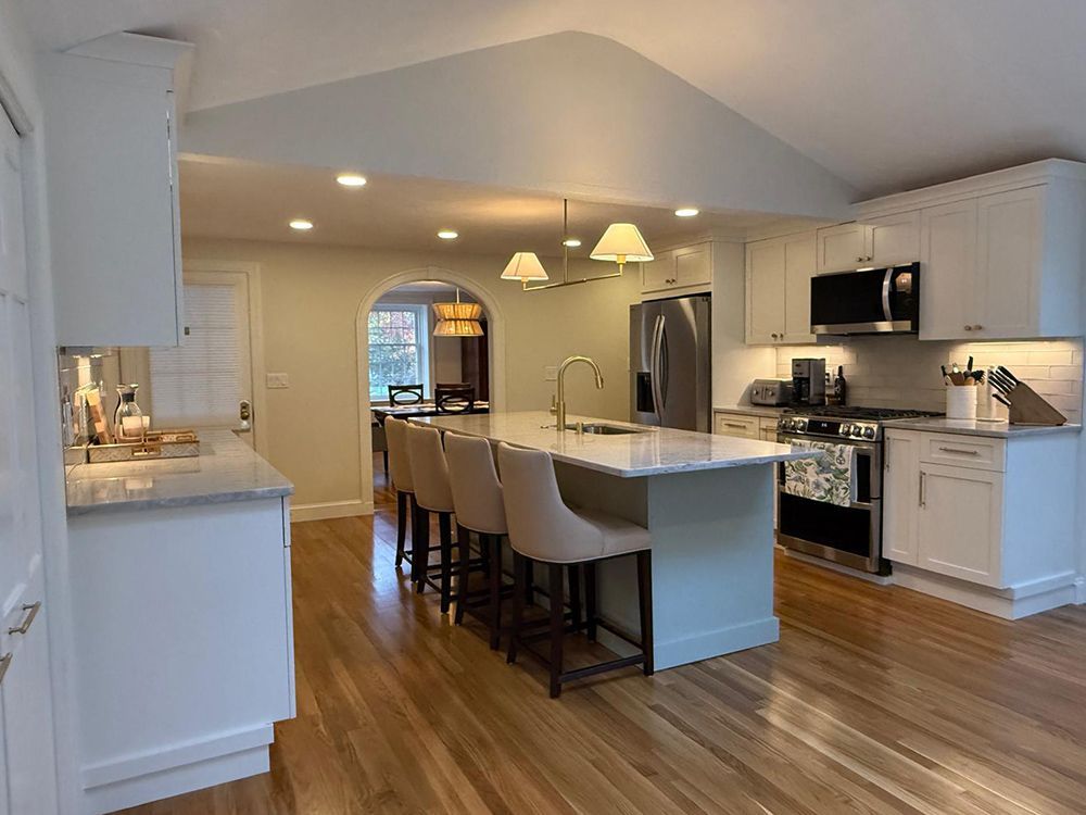 Spacious white kitchen with island, stainless steel appliances, wood floors, and arched doorway to dining area.