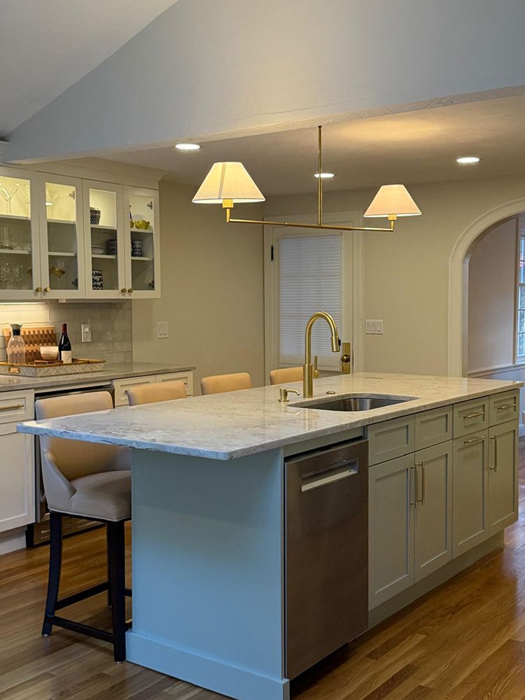 Kitchen with a light green island, marble countertop, gold faucet, and pendant lights.