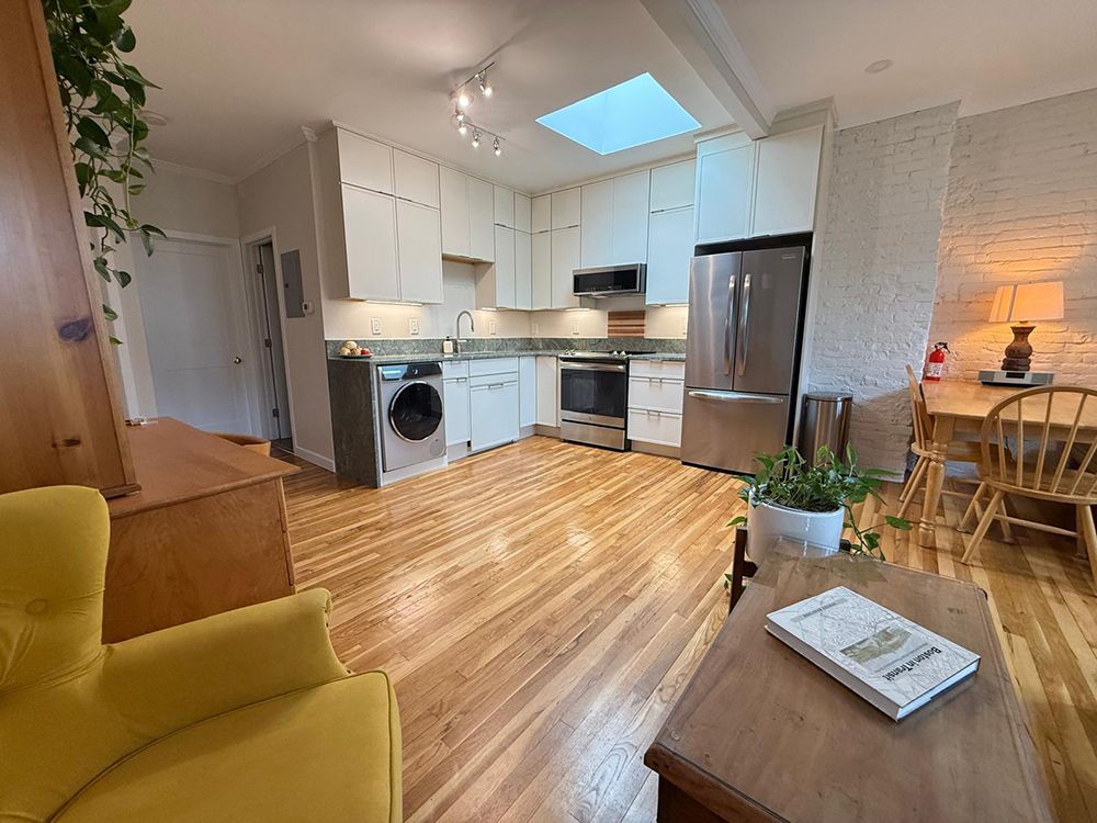 Cozy apartment kitchen with white cabinets, stainless steel appliances, and a wooden floor.