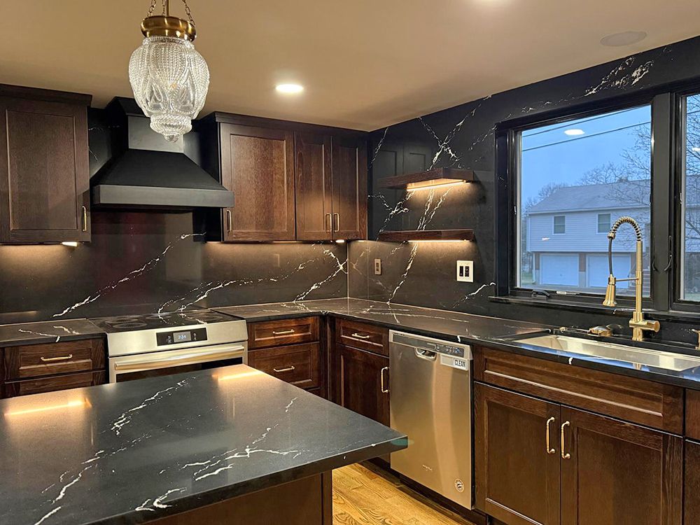 Modern kitchen with dark wood cabinets, black countertops with white veining, and a stainless steel sink and appliances.