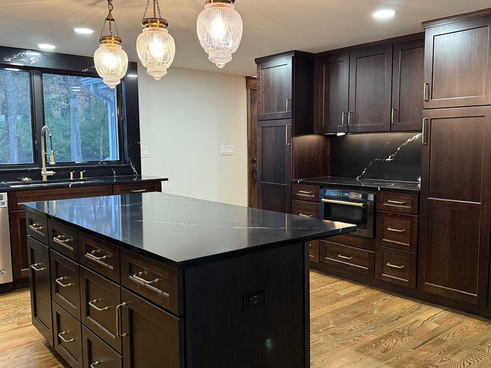 Dark wood kitchen with black countertops and island, pendant lights, and light wood floor.