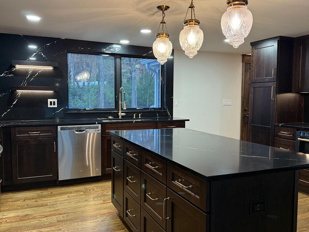Dark kitchen with island, cabinets, and marble backsplash; pendant lights hang above island.