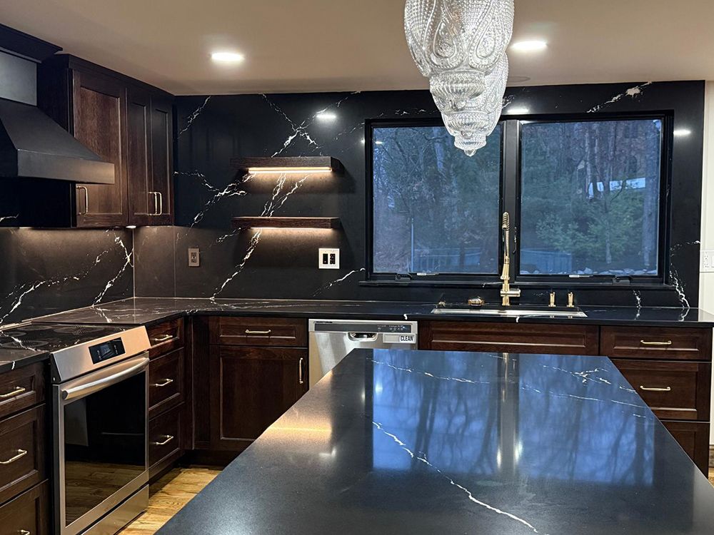 Kitchen with dark cabinetry, black countertops with white veining, stainless steel appliances, and a large window.