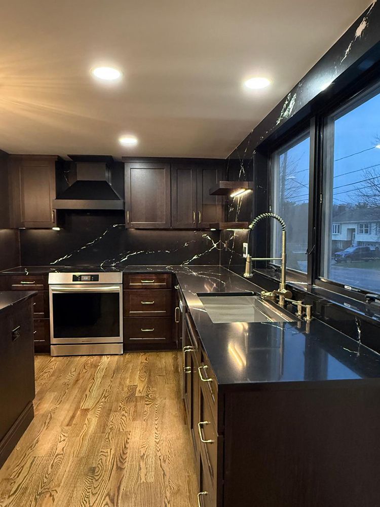 Modern kitchen with dark brown cabinets, black countertops, and gold hardware.
