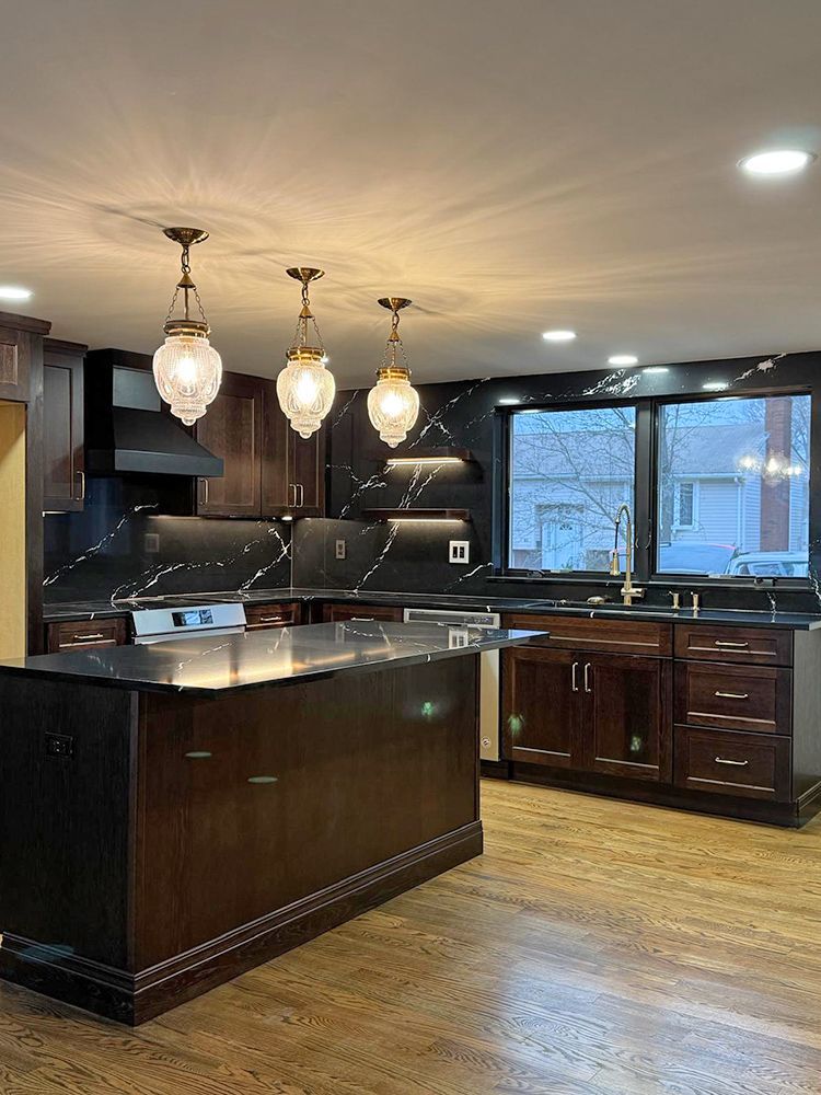 Dark wood kitchen with island, black countertops, three pendant lights, and a window.