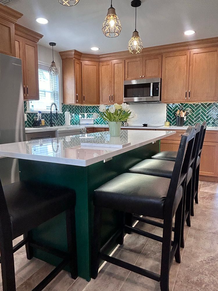 Kitchen with green island, wood cabinets, green backsplash, and black bar stools.