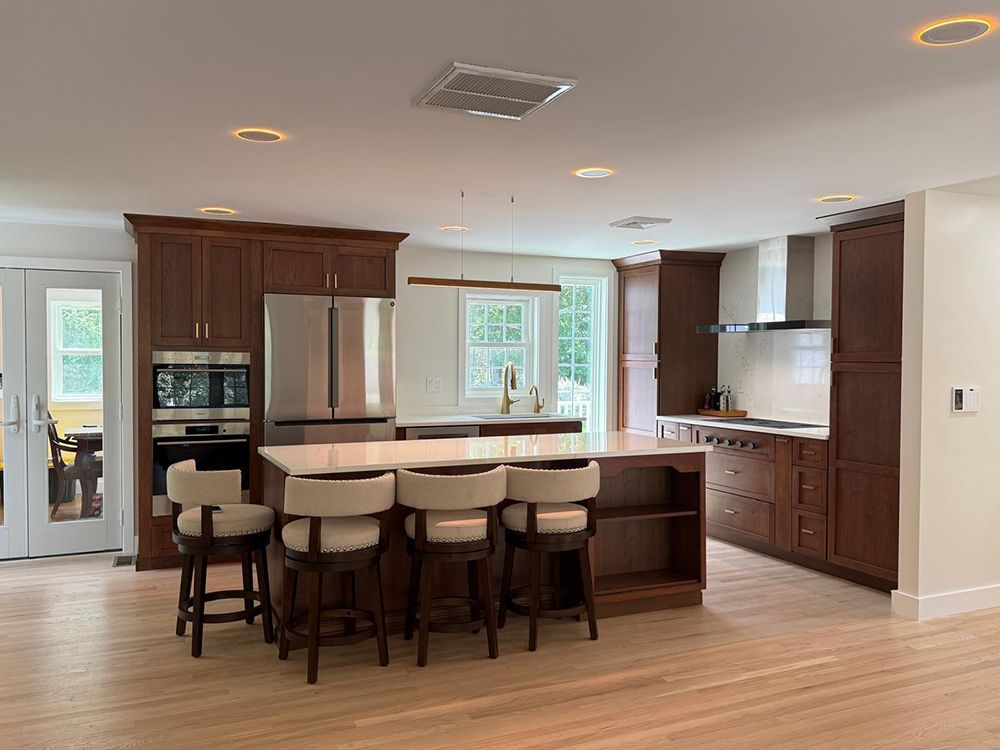 Spacious kitchen with island and barstools, dark wood cabinets, stainless steel appliances, and light wooden floors.