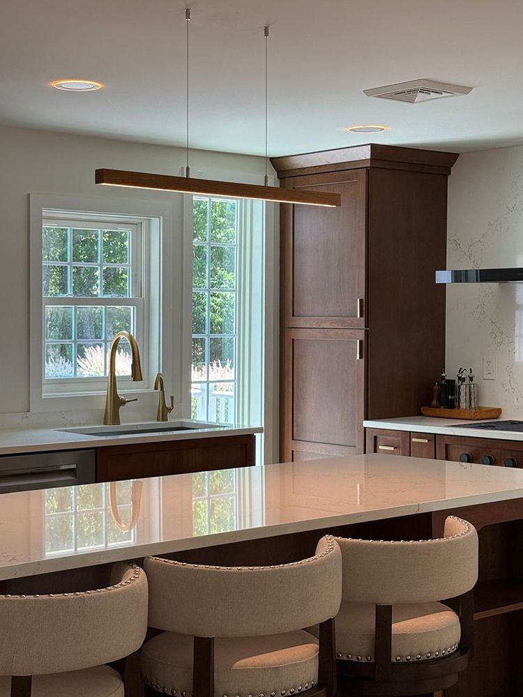 Kitchen with island and bar stools, wood cabinets, and a linear pendant light.