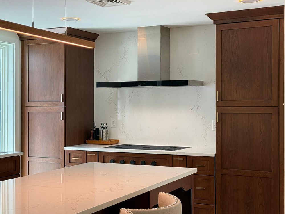 Kitchen with dark wood cabinets, white countertops, stainless steel range hood, and island.