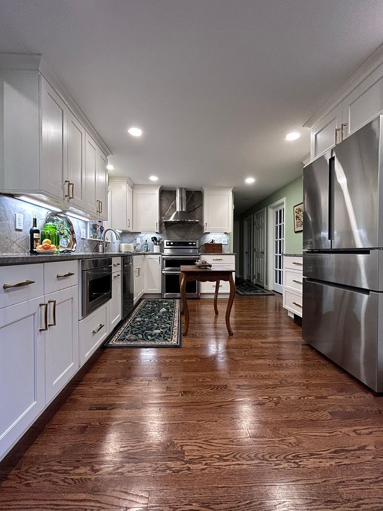 White kitchen with wood floors, stainless steel appliances, and a decorative rug.